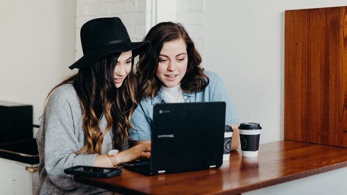 Friends creating fashion style boards together using a laptop in a cafe