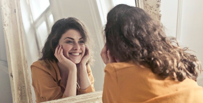 Consumer repeating positive affirmations to stop buying clothes, in front of a mirror