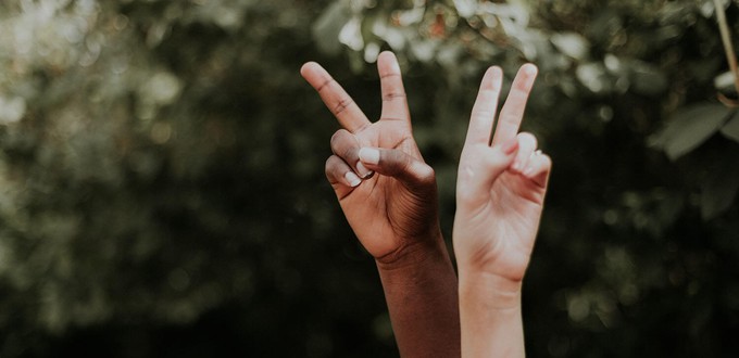 White and black hand doing a peace sign to symbolise the fight against racism in fashion